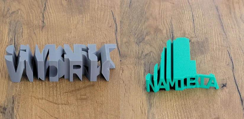 Two finished text-flip 3D prints on a wooden surface, one word-to-word and one word-to-shape
