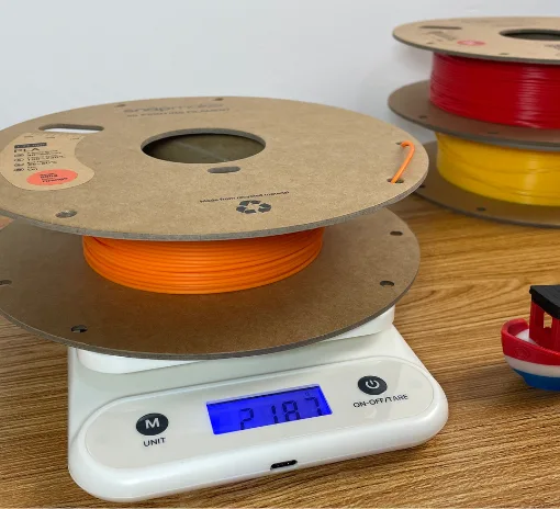 Partially used filament spool on kitchen scale with Benchy print for estimating remaining filament
