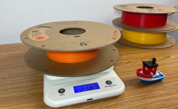 Partially used filament spool on kitchen scale with Benchy print for estimating remaining filament