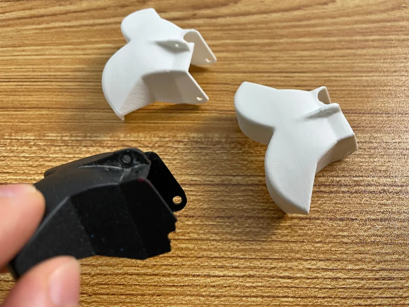 Broken RC boat reverse bucket next to two 3D printed replicas created from the scan