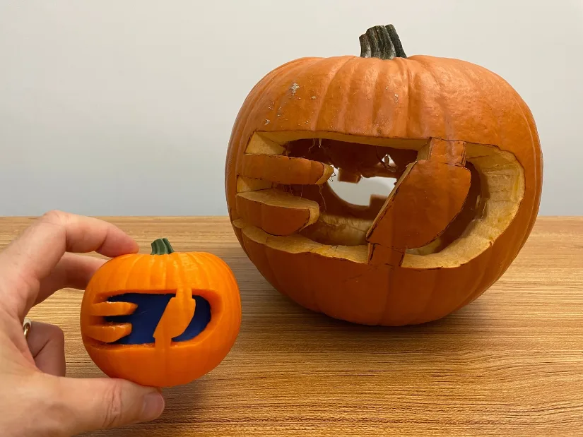 Back of carved pumpkin with 3DWithUs logo next to its multicolor 3D printed replica