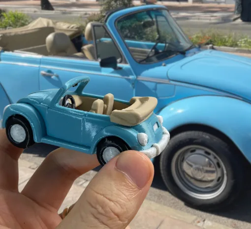 3D printed VW Beetle miniature created with Meshy AI in front of the original car